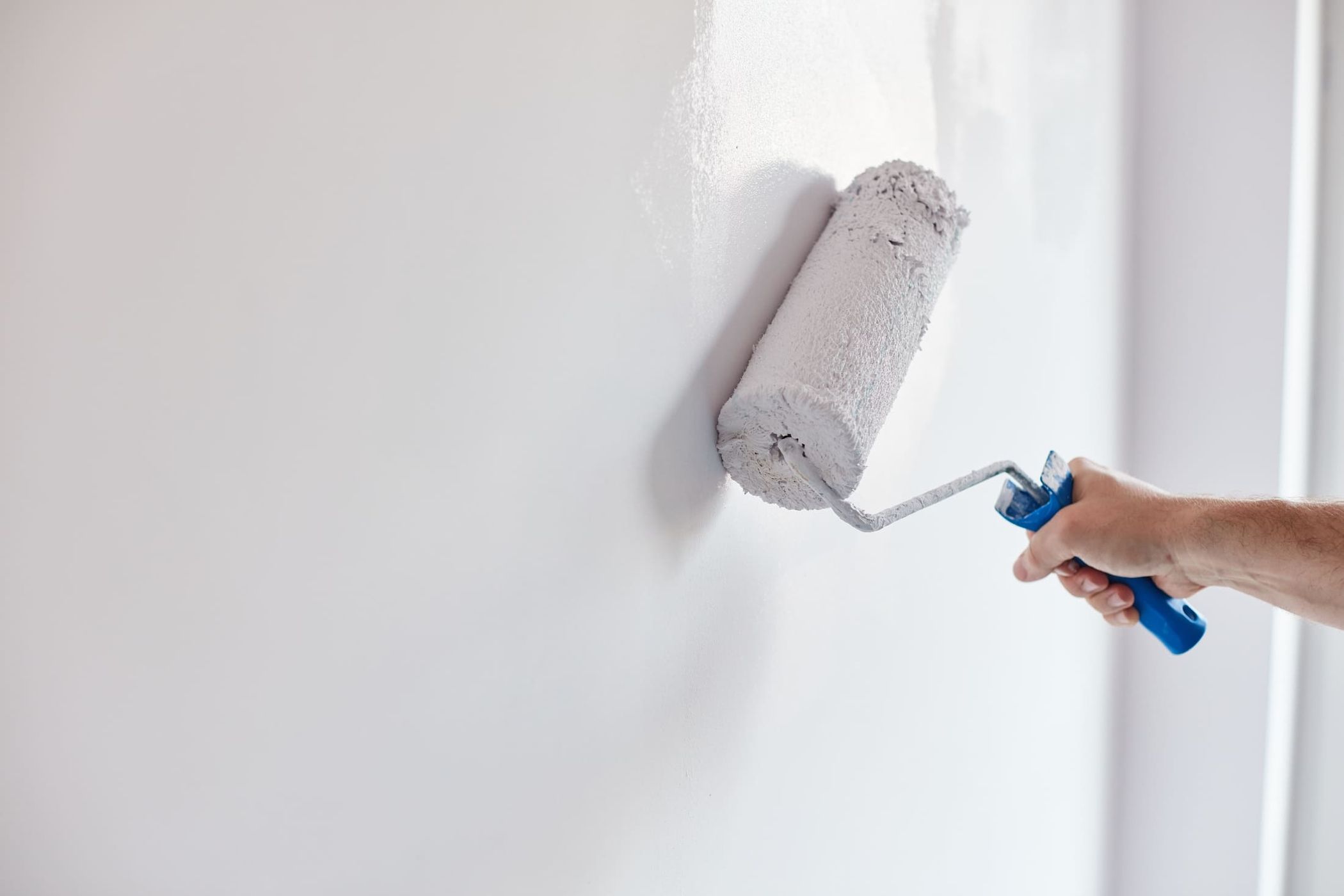 Person streicht eine Wand mit einer Farbrolle in hellem Weiß.